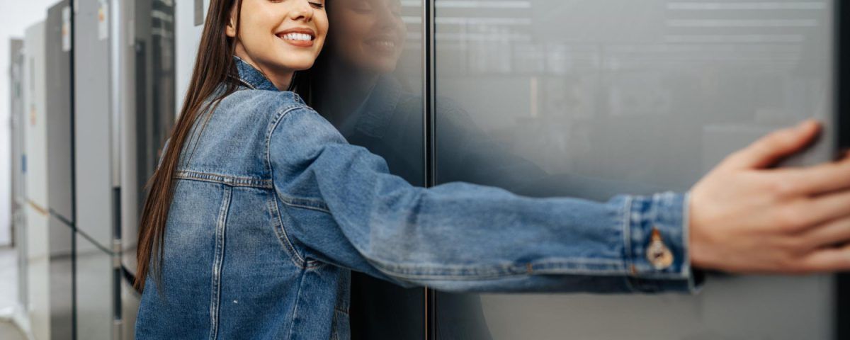 Cele mai bune frigidere, din anul 2026, îmbrățișate de o femeie. într-un magazin de electrocasnice.